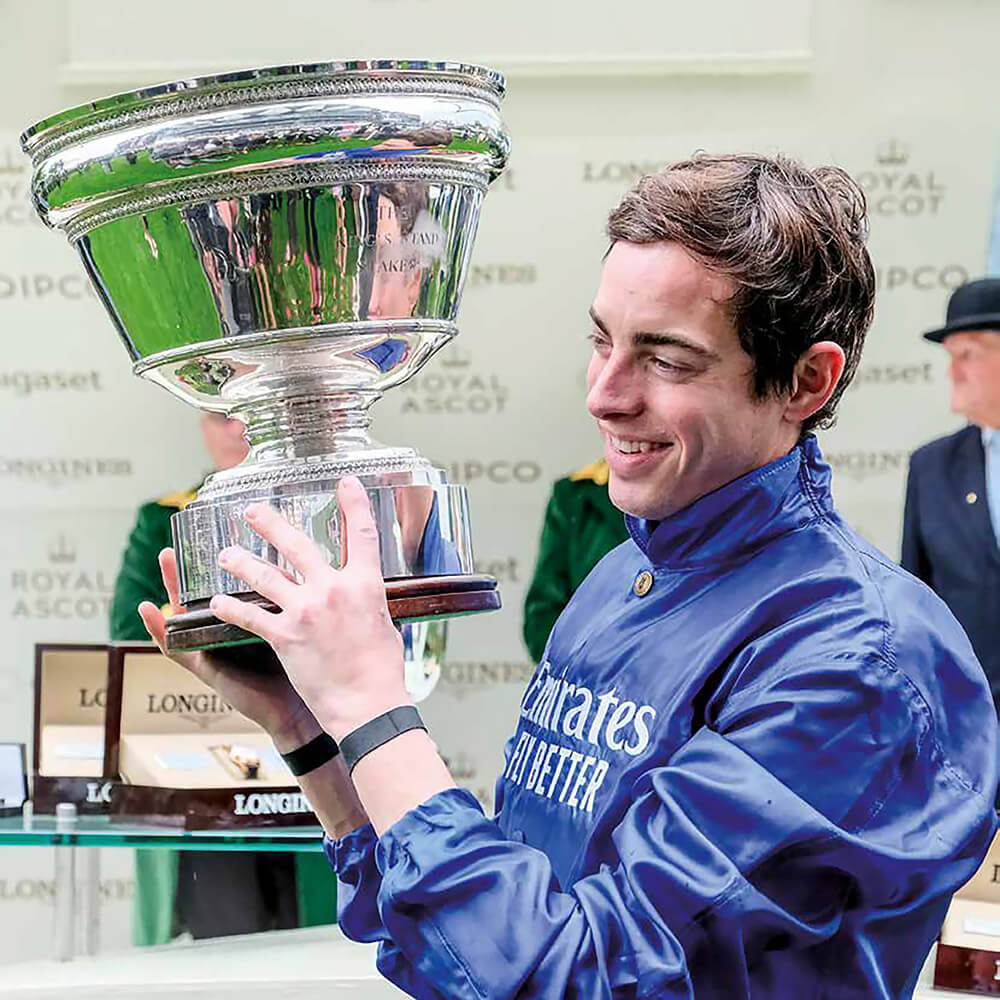 A winning jockey holding a Garrard trophy and smiling