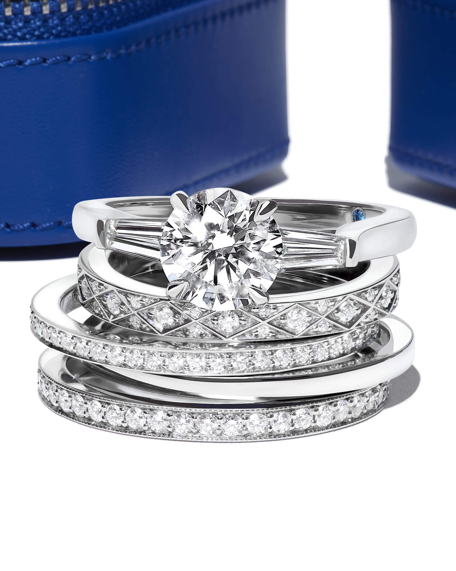 close up of a Garrard Charisma diamond engagement ring witha stack of wedding bands with a Garrard jewellery boxs b