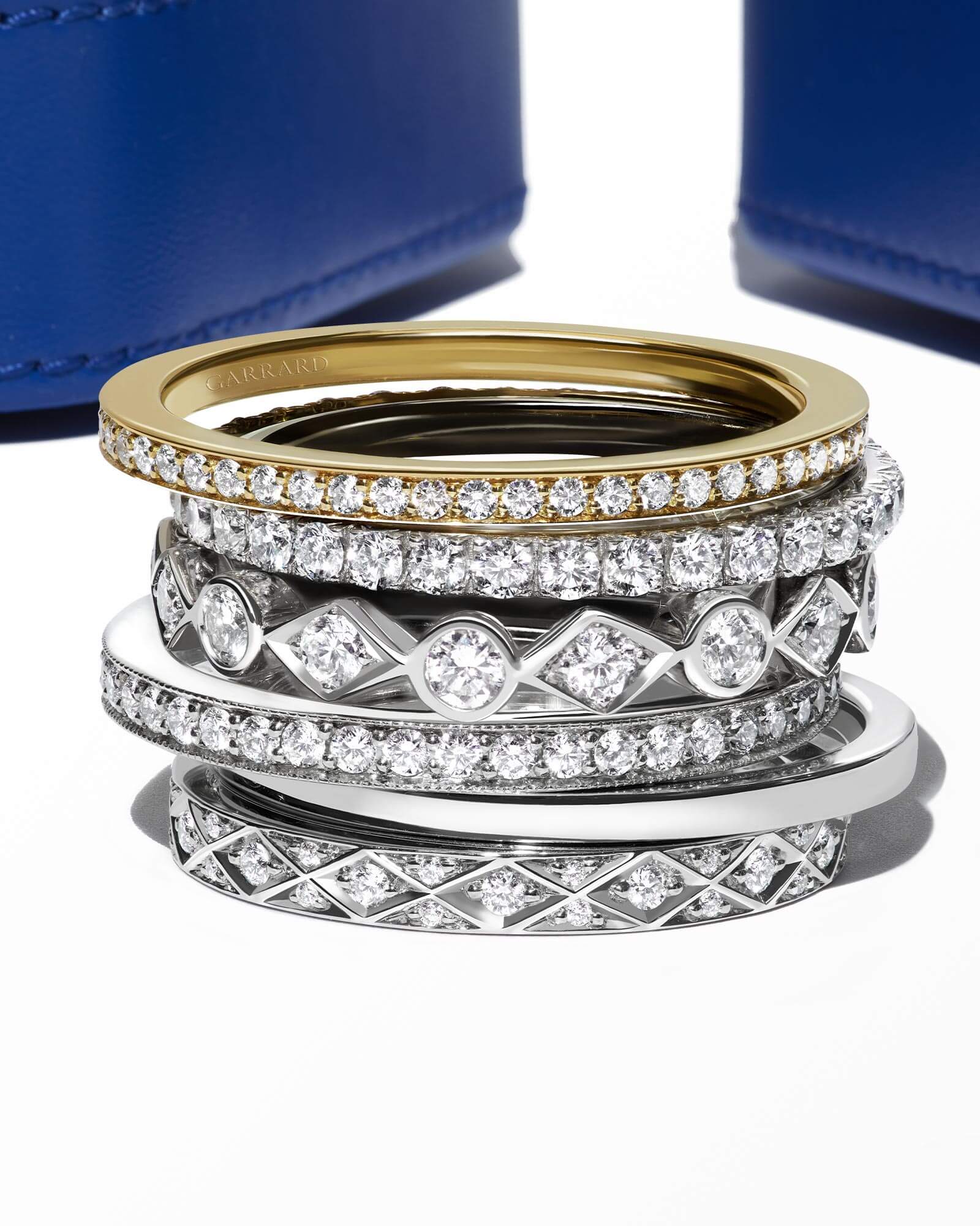 close up of a stack of Garrard diamond and plain wedding bands with Garrard jewellery boxs light grey bg